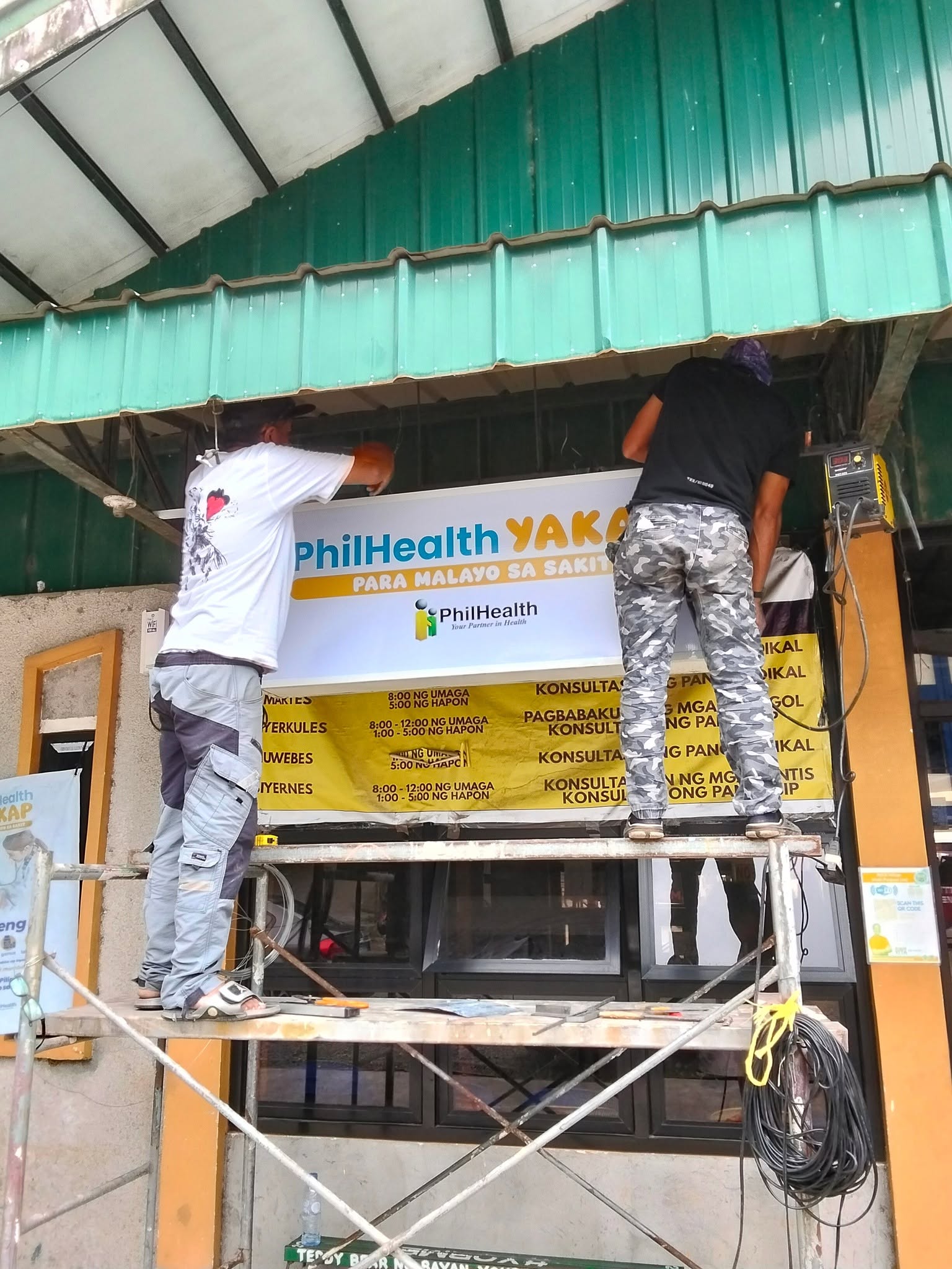 JM and Roldan putting on PhilHealth signage